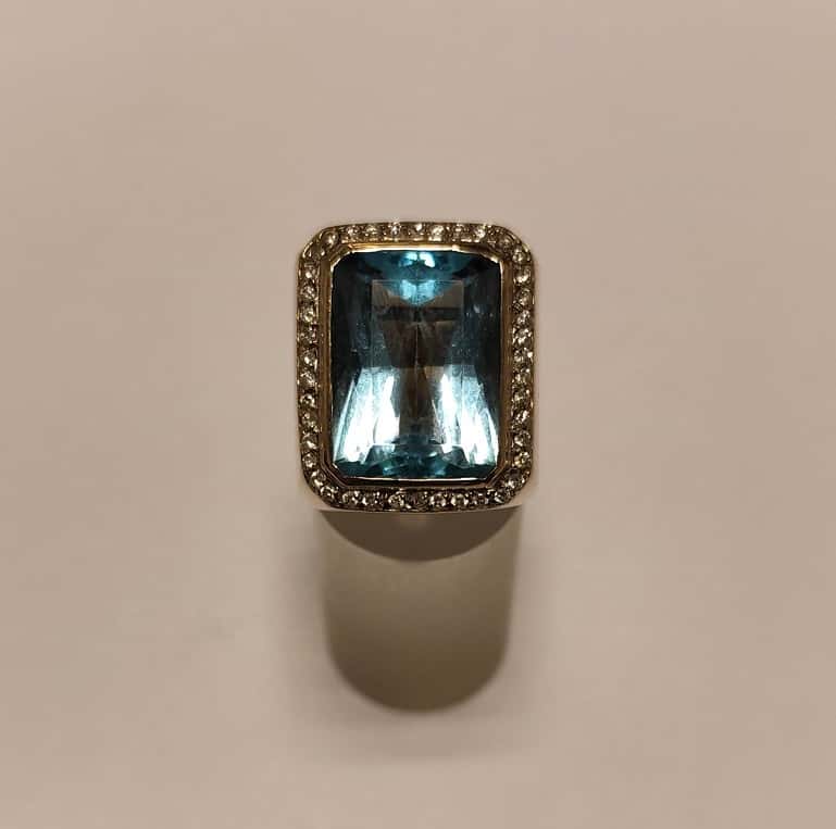 UN ANILLO REALIZADO EN ORO BLANCO KTE 18 CON BRILLANTES QTE. 0,40 TOTAL APROX.(DEFECTOS) Y TOPACIO CELESTE. (INF LAB 86356). MEDIDA 16. PESO APROX. 23,1 GRS. DETERIOROS EN GRAL.