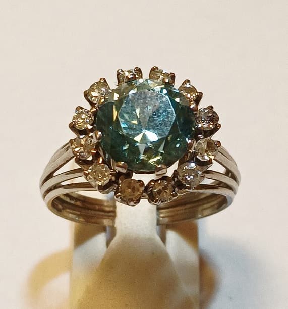 UN ANILLO REALIZADO EN PLATINO, CON ZIRCON CELESTE CENTRAL Y BRILLANTES CIRCUNDANTES QTE. 0.60 TOTAL APROX. (DEFECTOS). PESO 8.7 GRS. TOTAL APROX. MEDIDA 19 APROX. INFORME LABORATORIO DE GEMOLOGIA NRO. 86761.