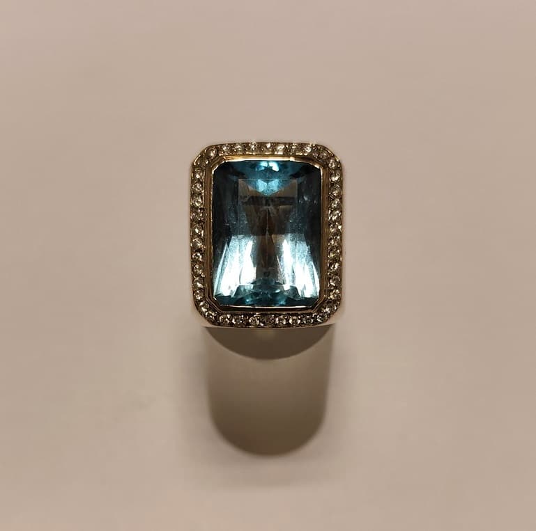UN ANILLO REALIZADO EN ORO BLANCO KTE 18 CON BRILLANTES QTE. 0,40 TOTAL APROX.(DEFECTOS) Y TOPACIO CELESTE. (INF LAB 86356). MEDIDA 16. PESO APROX. 23,1 GRS. DETERIOROS EN GRAL.