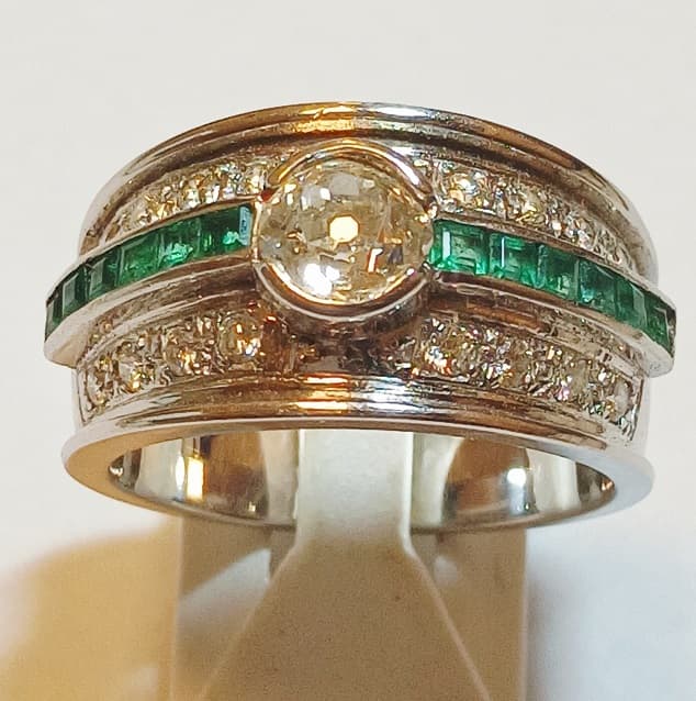 UN ANILLO REALIZADO EN ORO BLANCO KTE 18 CON BRILLANTE CENTRAL 0.65 APROX. Y BRILLANTES COMPLEMENTARIOS QTE 0.32 TOTAL APROX. CON PIEDRAS VERDES SIN POSIBILIDAD DE DETERMINAR PESO 9.5 GRS MEDIDA 20
